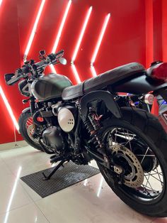 a black motorcycle parked in front of a red and white wall with lights behind it