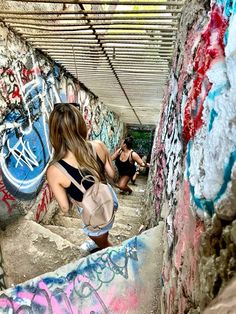 a woman sitting on the ground in an alley with graffiti all over her walls and floor