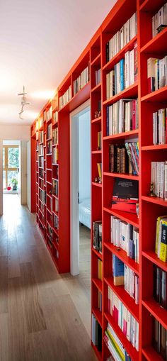 a long red bookcase filled with lots of books next to a doorway that leads to another room