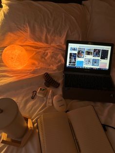 a laptop computer sitting on top of a bed next to an open notebook and other items