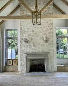 an empty living room with stone fireplace and wood beamed ceiling, surrounded by windows