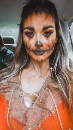 a woman with painted face and makeup in the back seat of a car, wearing an orange top