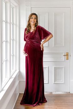 a woman in a long red dress standing next to a white door and smiling at the camera