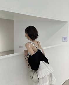 a woman in a white dress leaning against a wall with her back to the camera