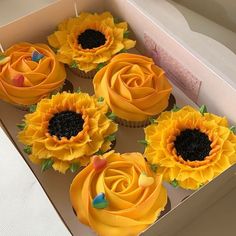 cupcakes with yellow frosting and sunflower decorations in a box on a table