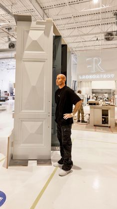 a man standing next to a tall white pillar in a room filled with other items