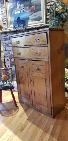 an old wooden cabinet is in the middle of a room with hardwood floors and paintings on the wall