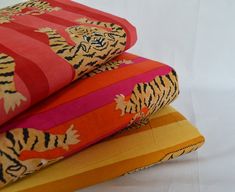 three pillows are stacked on top of each other, one with a tiger pattern and the other with an orange stripe