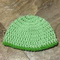 a green crocheted hat sitting on top of a stone floor