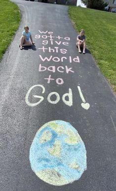 two children sitting on the side of a road with chalk written in front of them