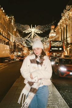 a woman is standing on the street with her arms crossed and wearing a white coat