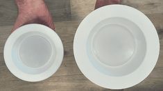 two white plates being held by hands on a wooden floor