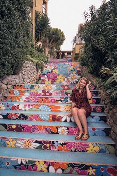 a woman is sitting on the steps painted with flowers and plants in front of her