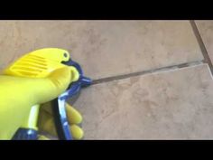 a person with yellow gloves and blue handles cleaning tile on the floor next to a spatula