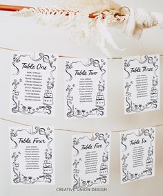 wedding seating cards hanging on a rope in front of a white backdrop with black and white designs