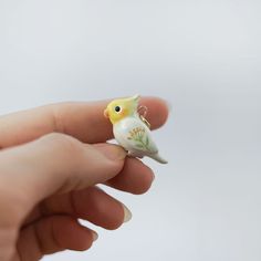 a tiny yellow bird sitting on top of a persons finger in front of a white background