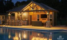 an outdoor bar next to a swimming pool at night with lights on and chairs around it