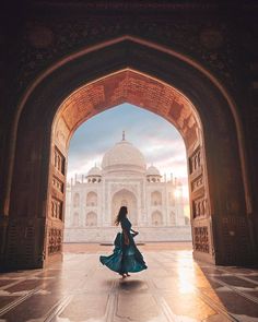 a woman in a blue dress is walking through an archway to the tajwa