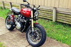 a red motorcycle parked on top of a sidewalk next to a wooden fence and grass