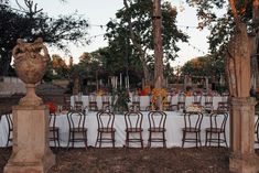 an outdoor dining table set up with white linens and flowers on the table, surrounded by tall trees