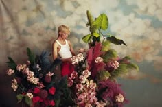 a woman sitting on top of a large bouquet of flowers next to a green plant