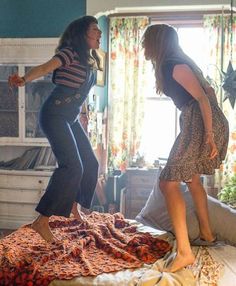 two women standing on top of a bed next to each other in a room with curtains