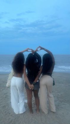 three women standing on the beach making a heart shape with their hands