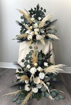 an arrangement of white flowers and greenery is displayed on a wooden floor in front of a wall