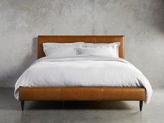 a bed with white linens and pillows in a gray room next to a concrete wall