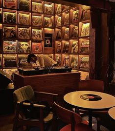 a man sitting at a table in front of a wall full of records and cds