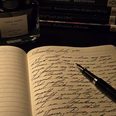 an open notebook with cursive writing on it next to a pen and inkwell