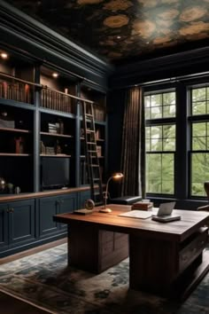 an office with dark blue cabinets and wooden desk in front of large window overlooking trees