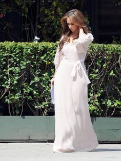 a woman in a white dress is walking down the street with her hand on her head