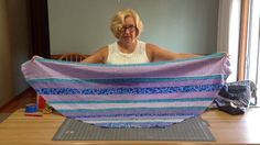 an older woman sitting at a table with a large quilt on it's back