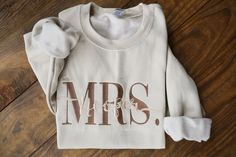 a white sweatshirt with the word mrs on it sitting on top of a wooden floor