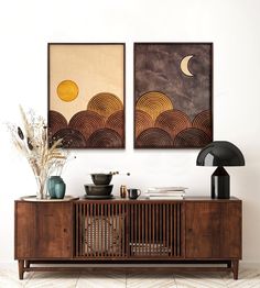 two paintings hang on the wall above a wooden sideboard with vases and plants