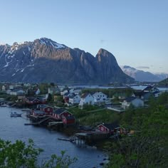 a small village on the shore of a body of water with mountains in the background