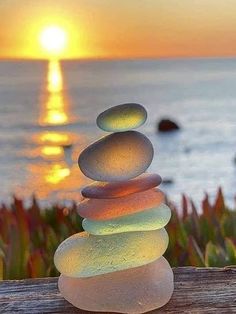 a stack of rocks sitting on top of a wooden table next to the ocean at sunset