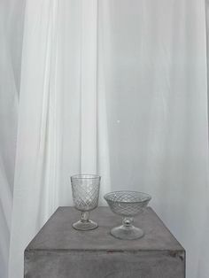 two glass bowls sitting on top of a wooden table next to a white drapes