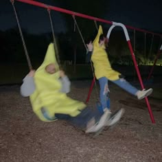 two children swinging on swings at night