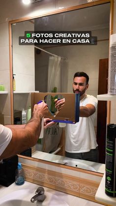 a man taking a selfie in front of a bathroom mirror while holding a cardboard box