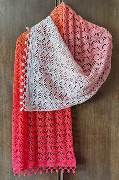 two crocheted shawls hanging on a wooden door, one in pink and the other in red