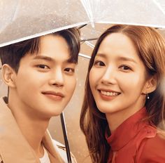 a man and woman under an umbrella smiling at the camera while standing next to each other