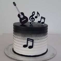 a black and white cake with musical notes on top, sitting on a plate next to a guitar