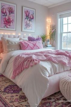 a white bed with pink comforter and pillows in front of a large window filled with lights