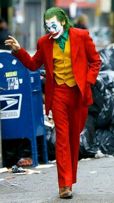 a man in a red suit and clown makeup walking down the street with his hands out