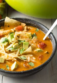 a bowl of soup with tortilla chips and avocado on the side