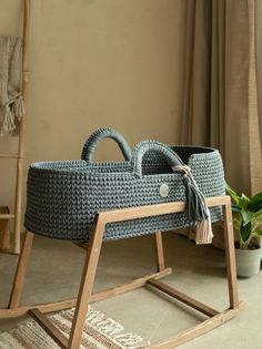 a crocheted baby's cradle sitting on the floor next to a potted plant