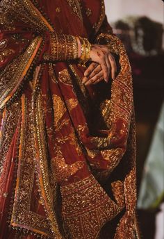 a woman in a red and gold outfit with her hands on her chest, holding the other