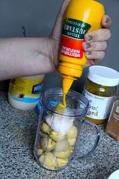 a person pouring mustard into a blender filled with potatoes and onions on top of a counter